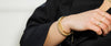 Wrist showing curated Loretana 14K gold bracelet stack on black blazer, interchangeable vs charm bracelet comparison. Hallmarked Kaunas piece.
