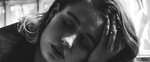 Black and white intimate portrait of Loretana model with hand to face against glass blocks, sterling silver hoop earrings guide. Kaunas.