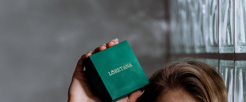 Loretana model holding branded green jewelry box high against glass block wall, complete sterling silver gift guide. Hand-finished Kaunas.