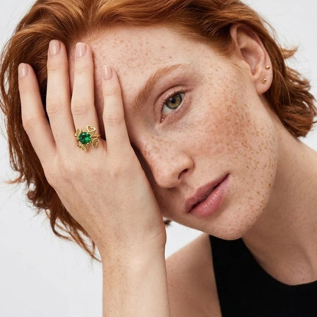 Red-haired woman with her hand over one eye wearing the 14K gold-plated Interchangeable Stone Heart Ring with a green AAAAA cubic zirconia