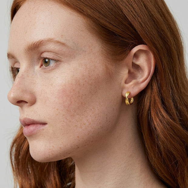 Model wearing twisted knot huggie hoop in 14K gold-plated 925 silver