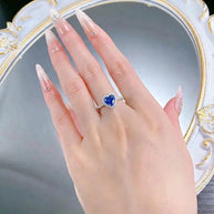 Hand wearing the Blue CZ Heart Ring in rhodium-plated 925 sterling silver: a heart-cut blue AAAAA cubic zirconia in a pavé halo, the colour worn for protection.