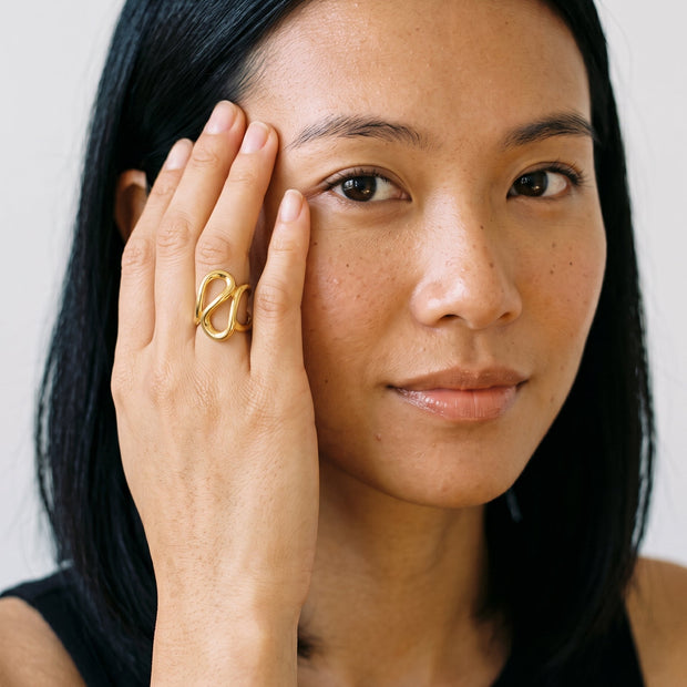 Model with hand at the temple wearing the chunky 14K gold-plated 925 silver geometric figure-8 open ring.