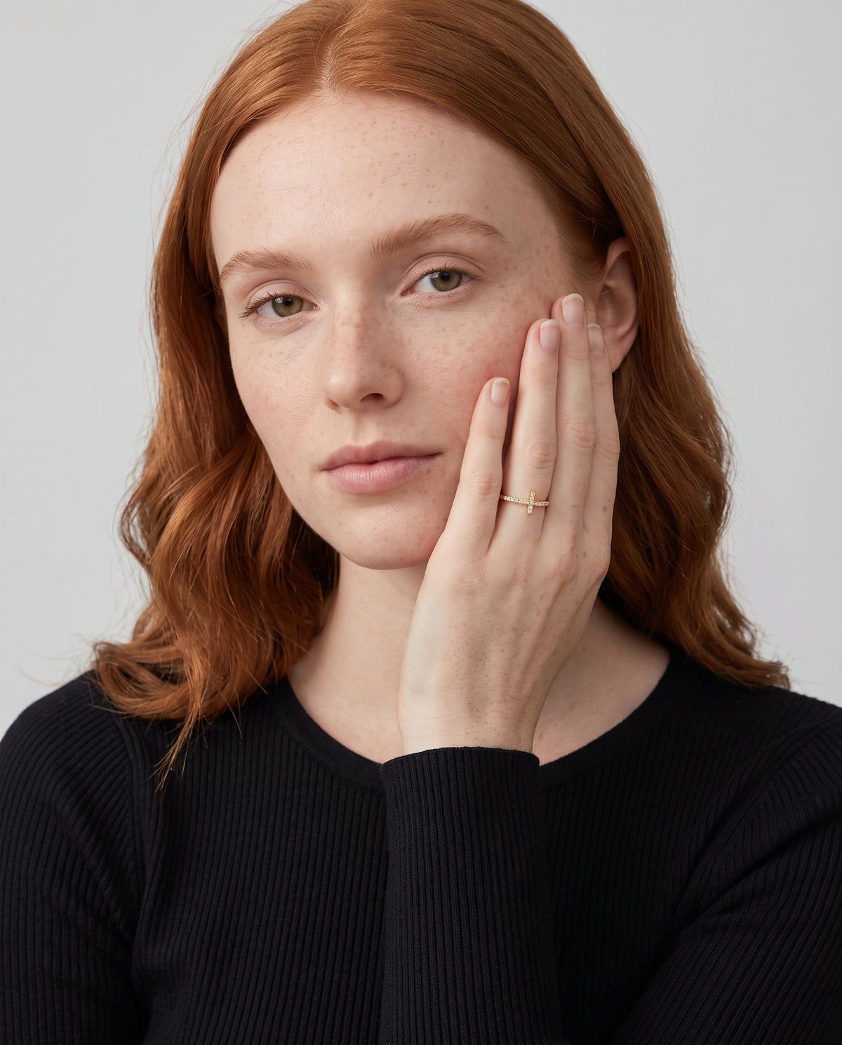 Model wearing the 14K gold-plated sideways cross ring with white CZ, hand against her cheek
