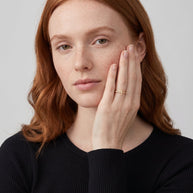Model wearing the 14K gold-plated sideways cross ring with white CZ, hand against her cheek