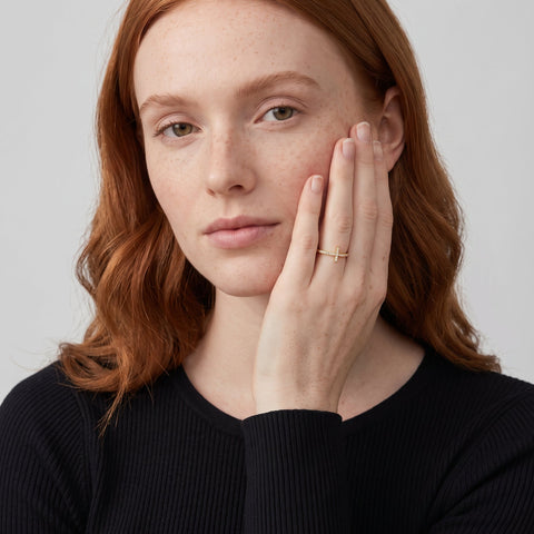 Model wearing the 14K gold-plated sideways cross ring with white CZ, hand against her cheek