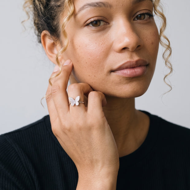 Model with curly hair wearing the 925 silver butterfly ring, pave CZ wings across the finger, hand resting at the jaw.